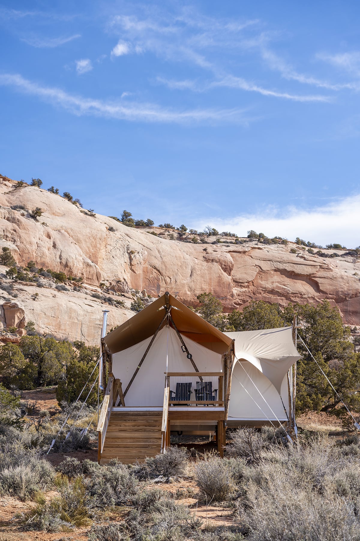 A glamping tent with a deck and chairs, set against a desert mountain backdrop.