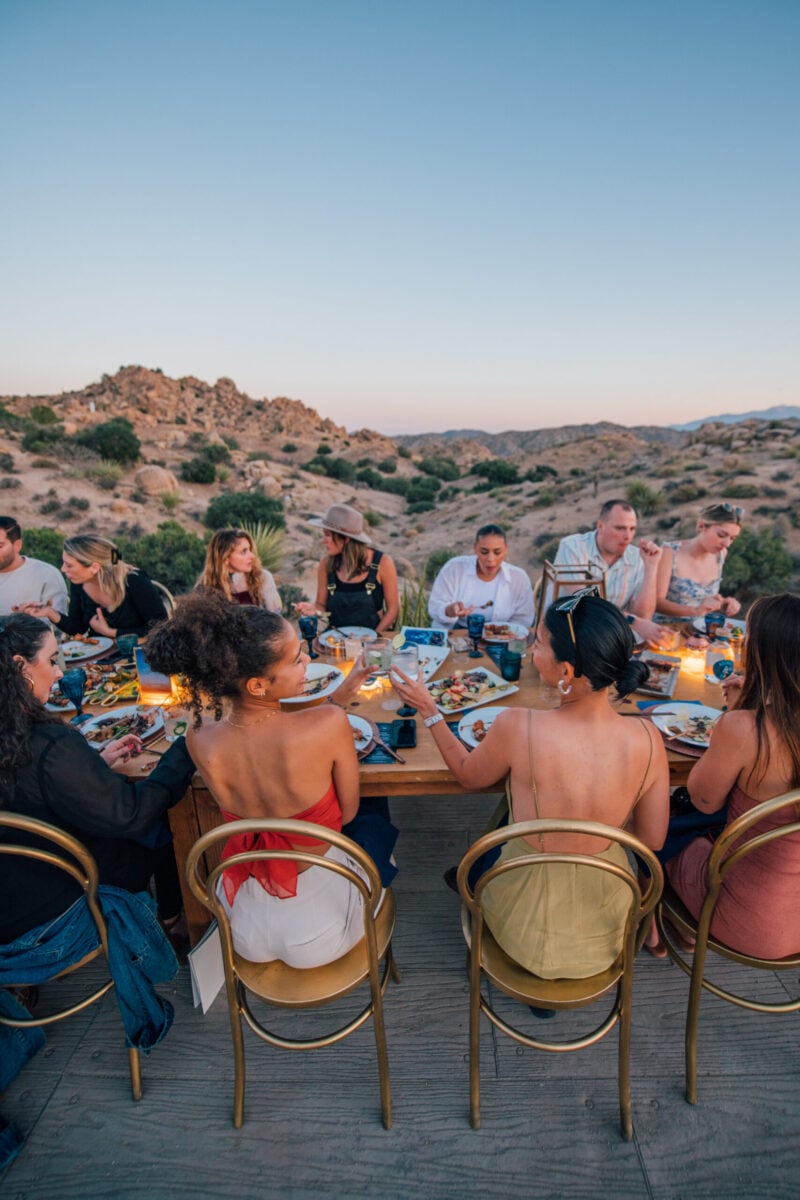 A group of people sitting around a table outdoors in a desert landscape
