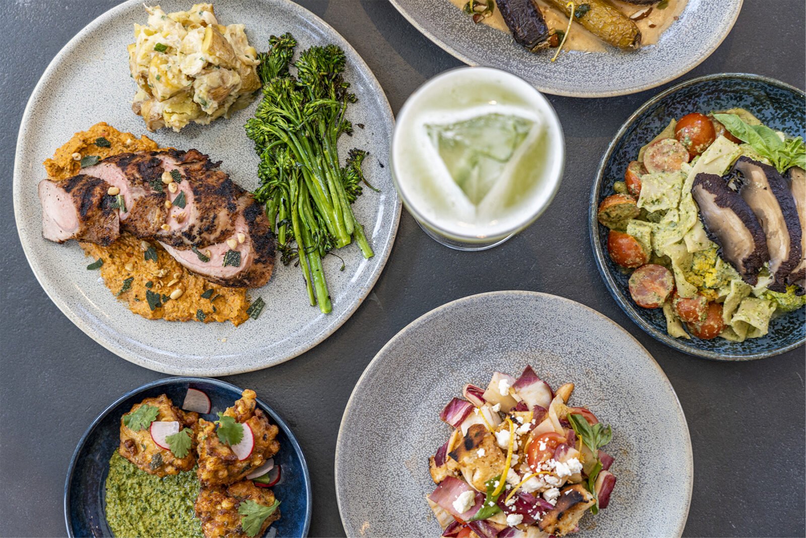 Plates of ham, cheesy potatoes, a colorful salad, and a fresh pasta dish, examples of ULUM's on-site cuisine, arranged on a table.
