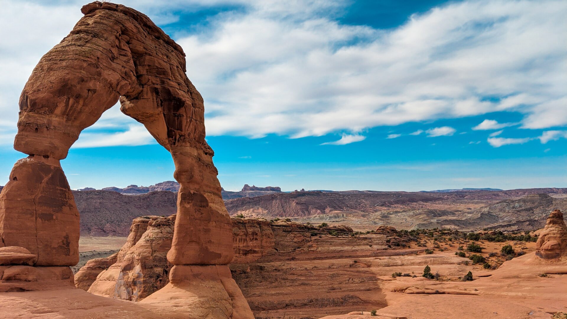Delicate Arch in Arches National Park in the foreground with red rocks and snow-capped mountains in the background.