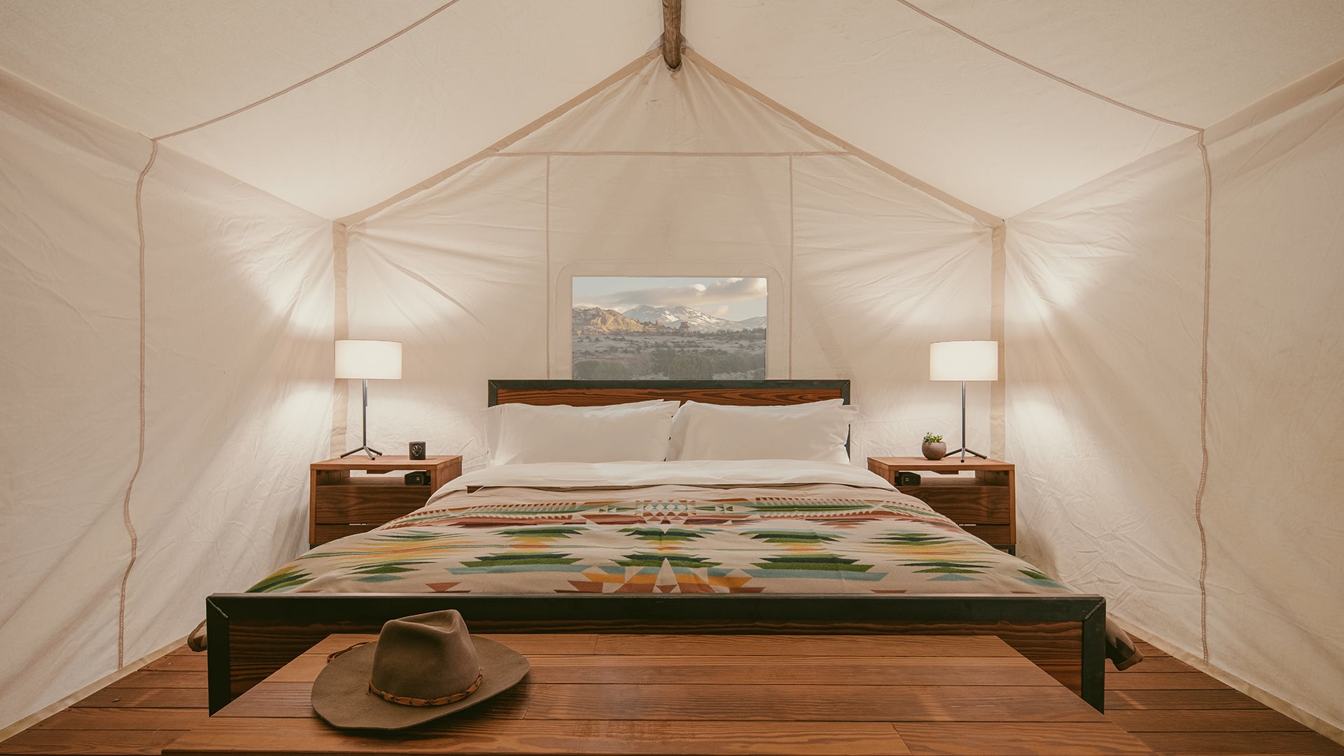 A glamping tent with a large bed, wooden furniture, and a view of mountains.