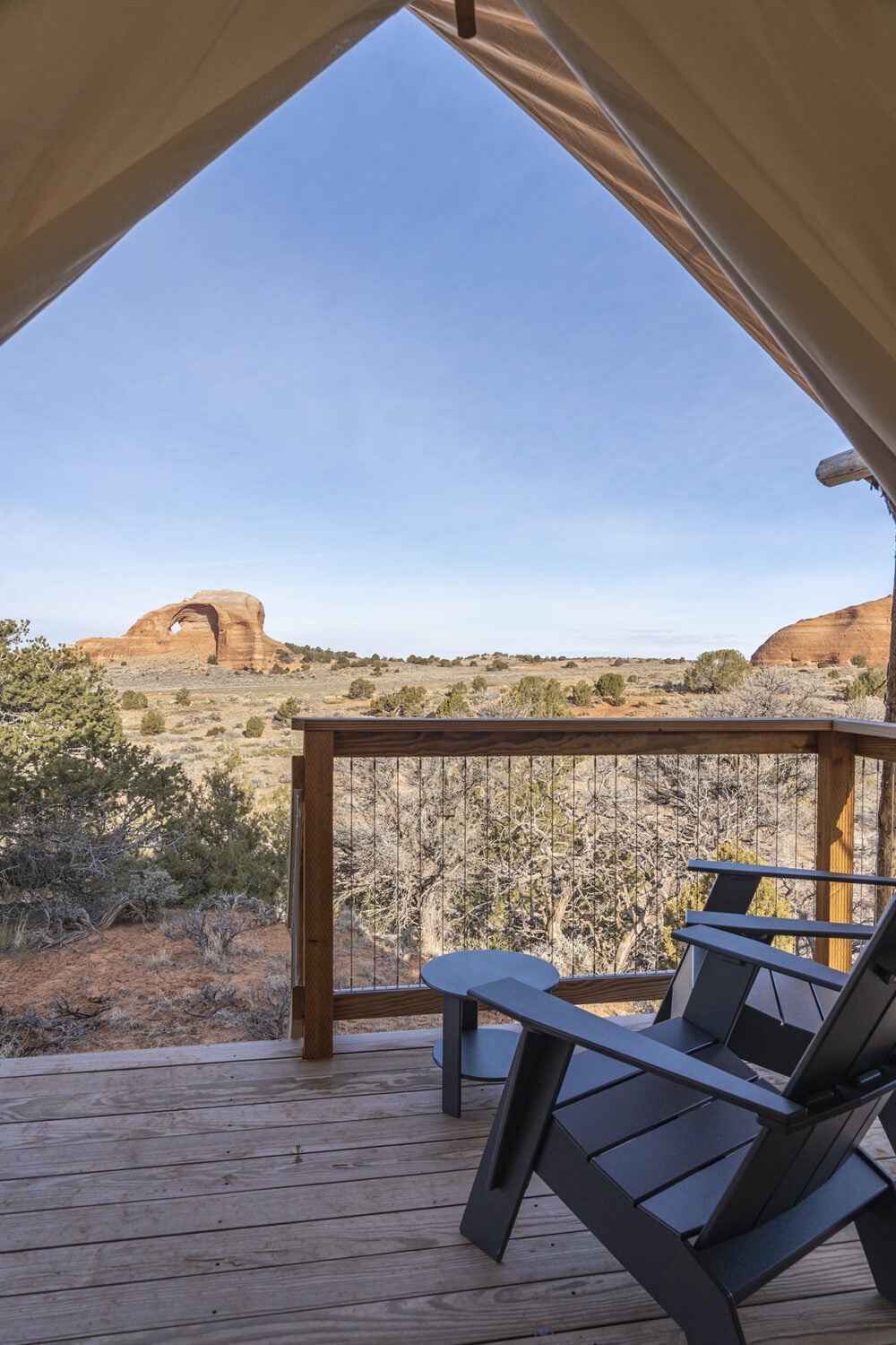 A balcony with a wooden deck and metal railing overlooking a desert landscape with a prominent rock formation in the distance.