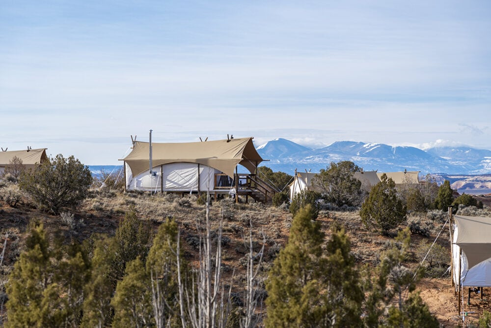 A tented structure with a wooden deck and stairs, surrounded by desert landscape and mountains in the background.