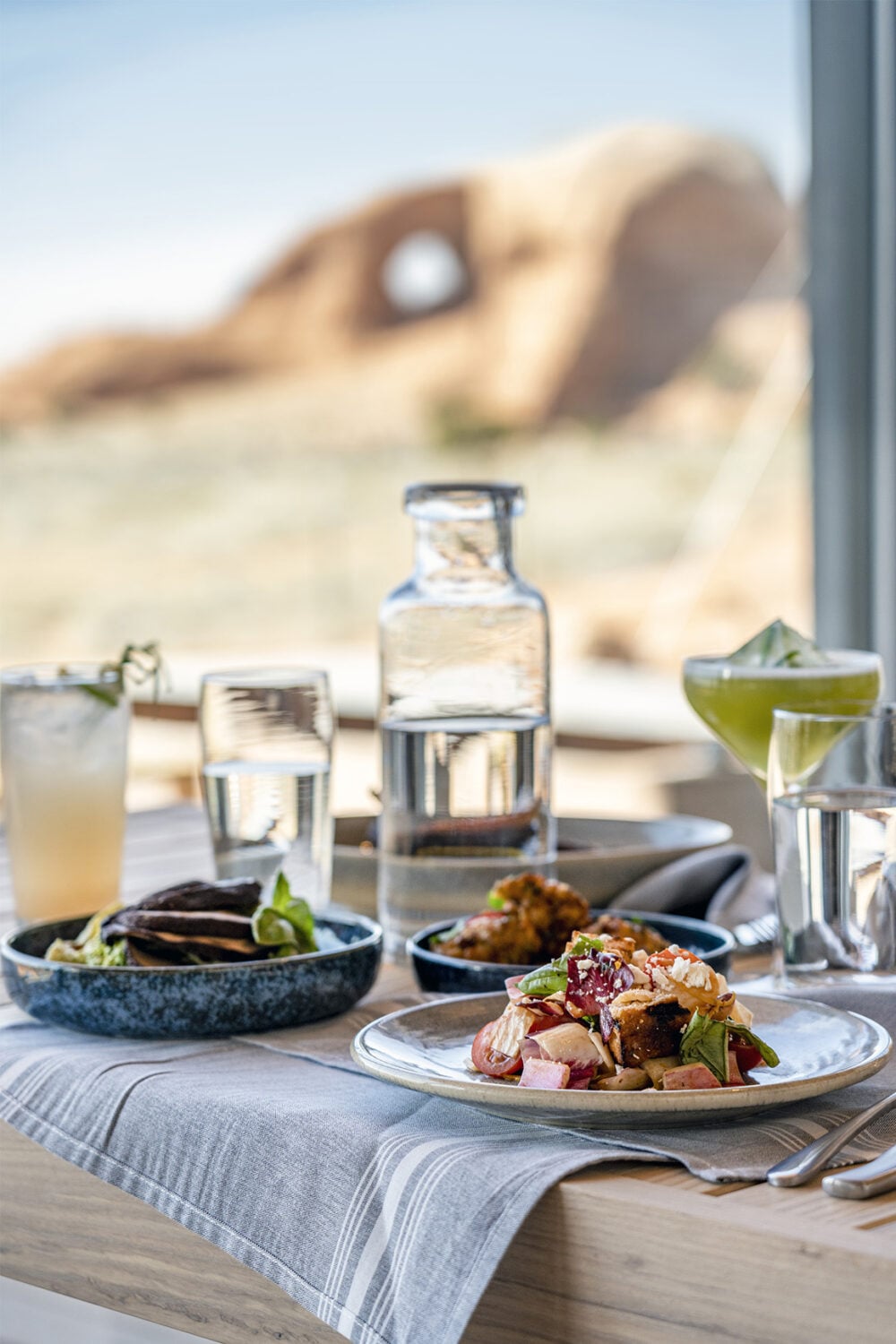 A table set with food and drinks in front of a window with a view of a desert landscape.