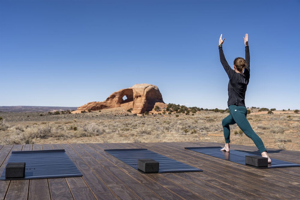 A woman performing yoga on a deck at ULUM Moab while surrounded by desert scenery