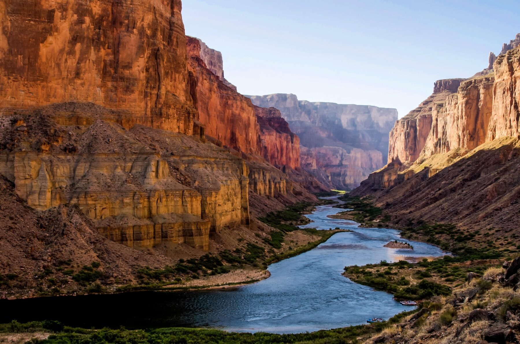 The Colorado River runs beneath towering sandstone cliffs.